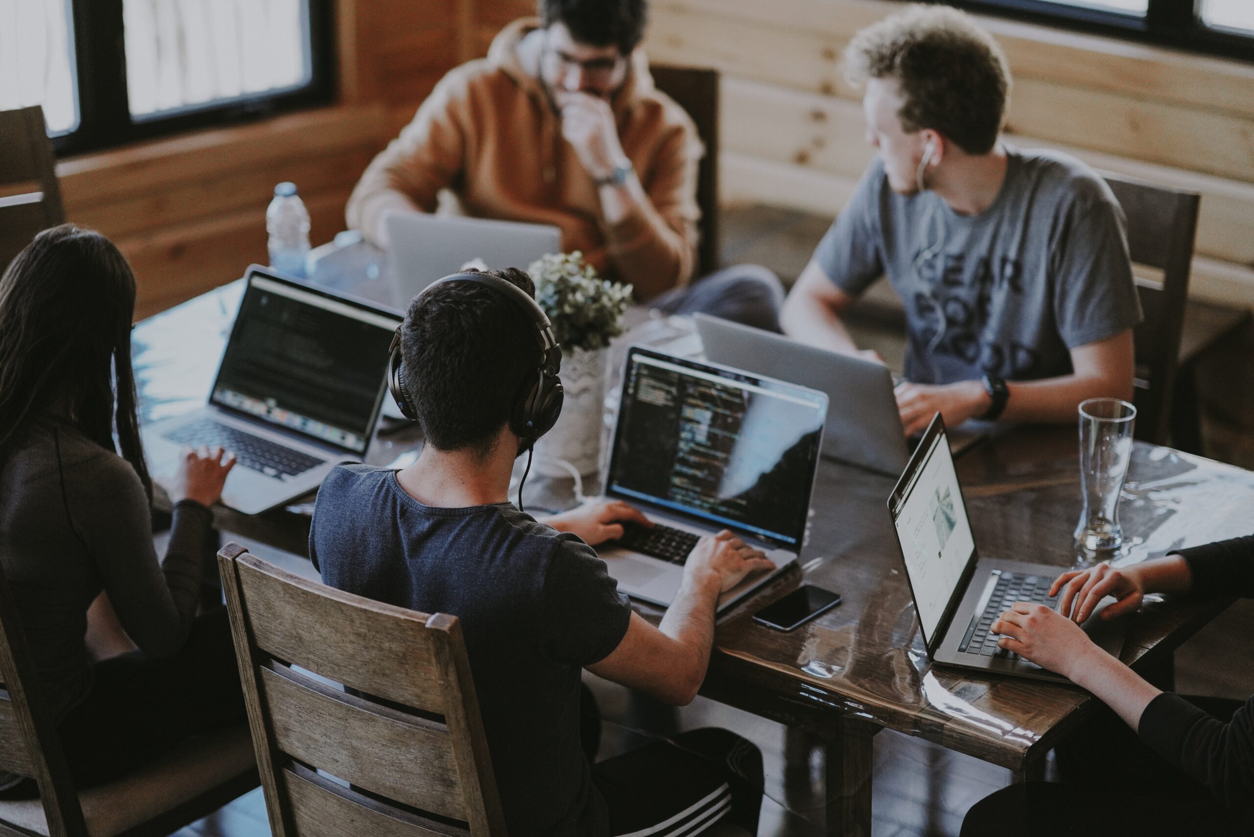 Employee engagement trends symbolised by a modern, hipster-looking bunch of 20-something year olds gathered on laptoops at a coffee table in a wood cabin/coffee shop. Image by Annie Spratt via Unsplash.